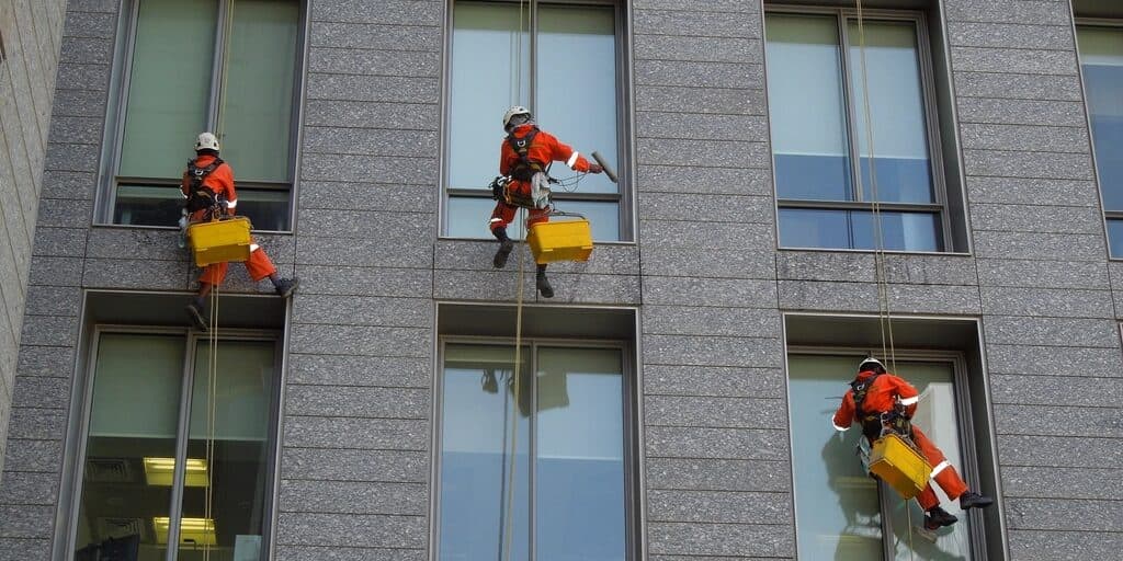 Reinigungskräfte in Schutzausrüstung reinigen die Fensterfront eines Bürogebäudes